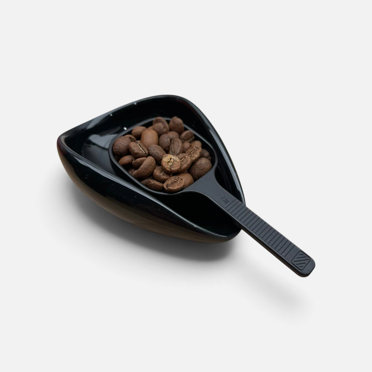 Kaffebønner i en måleskje som er oppi en sort design porselenskål.